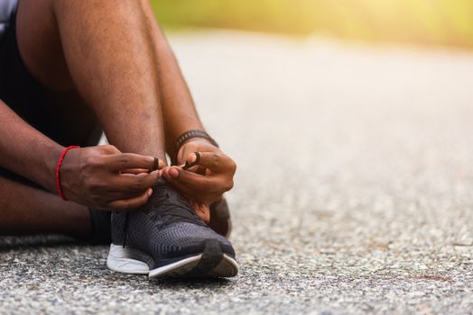 Close up Asian sport runner black man sitting shoelace trying running shoes getting ready for jogging and run at the outdoor street, health exercise workout concept