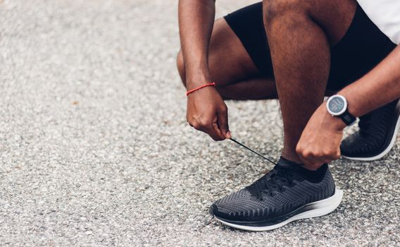 Close up Asian sport runner black man wear watch sitting he trying shoelace running shoes getting ready for jogging and run at the outdoor street health park, healthy exercise workout concept