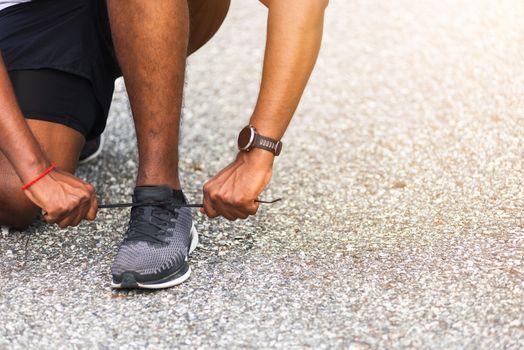 Close up Asian sport runner black man wear watch sitting he trying shoelace running shoes getting ready for jogging and run outdoor street health park with copy space, healthy exercise workout concept