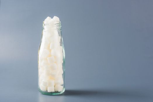 Glass bottle full of white sugar cube sweet food ingredient, studio shot isolated on gray background, health high blood risk of diabetes and calorie intake concept and unhealthy drink