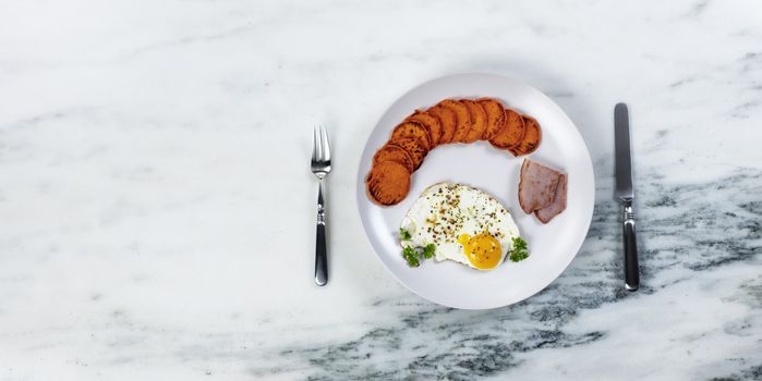 Serving plate filled with fresh breakfast consisting of healthy sweet potatoes, egg and fried ham 