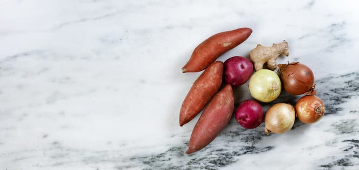 Fresh organic vegetables consisting of potatoes, onions and ginger root on marble stone