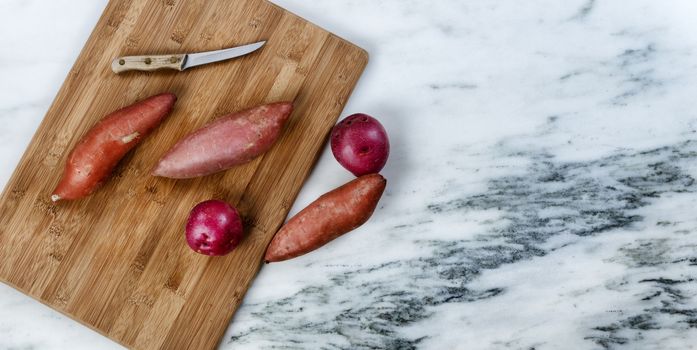 Fresh organic vegetables consisting of potatoes on marble stone with cutting board