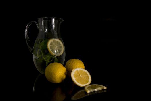 still life with a jug of water filled with mint and lemon with the raw lemon fruit in the foreground