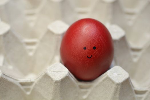 Red Easter egg with drawn smiling face on carton