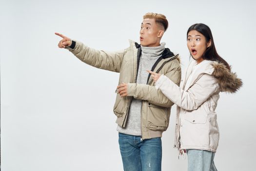 Young couple of Asian appearance in winter jackets dating surprise communication gray background