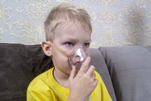 a 5-7 year old boy in a t-shirt takes an inhalation at home