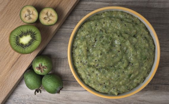 Ceramic bowl with mashed feijoa with kiwi and sugar on wooden table.