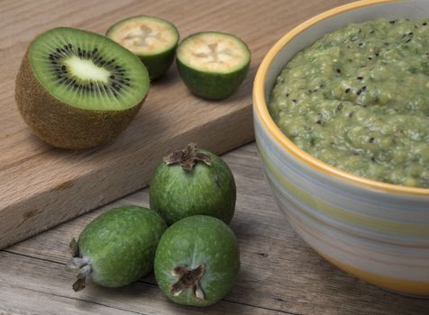 Ceramic bowl with mashed feijoa with kiwi and sugar on wooden table.