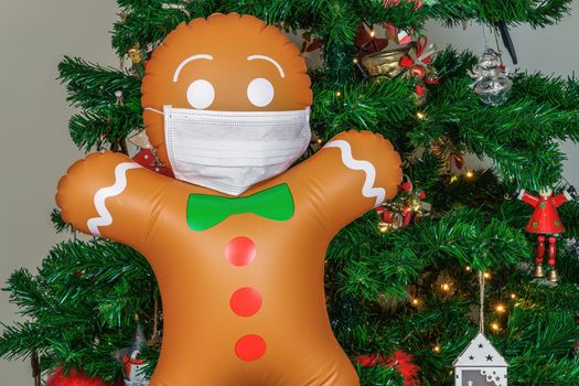 Air blown seasonal gingerbread figure before illuminated artificial decorated green tree with lights.