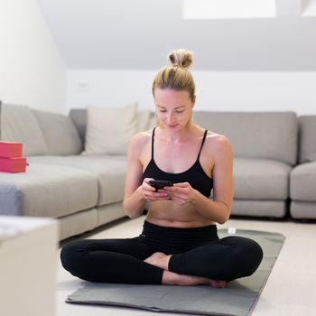 Beautiful blonde woman doing home workout indoors. Woman practice yoga at home. Fit girl using workout tutorials for healthy active lifestyle. Woman using quarantine for home workouts. Stretching