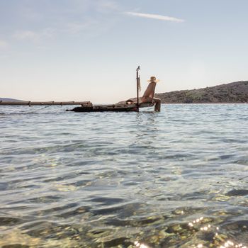 View of unrecognizable woman wearing big summer sun hat tanning topless and relaxing on old wooden pier in remote calm cove of Adriatic sea, Croatia.