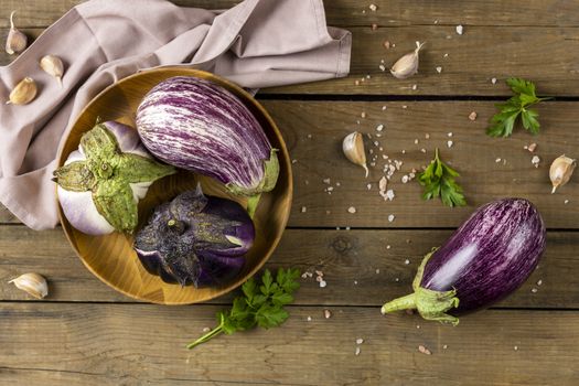 Wooden pot with different raw fresh eggplant. Dark wooden background. Concept of green house life style and products of subsistence farming, flat lay, copy space