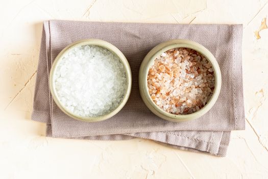 Pink Himalayan rock salt and white mineral salt in a ceramic bowls and spoon on a light background. Top view.