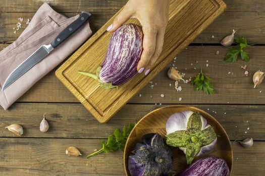 Woman hand hold raw fresh eggplant. Dark wooden background. Concept of green house life style and products of subsistence farming, flat lay, copy space