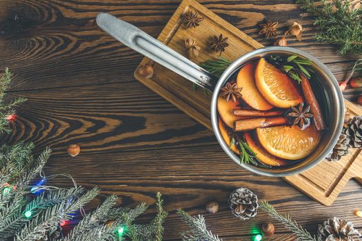 Christmas mulled red wine with the addition of spices and citrus fruits in a small metal pan on a rustic wooden table, top view. Pot of mulled wine, traditional christmas drink.