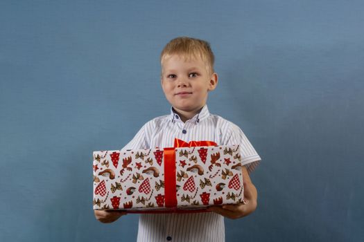 a boy in a shirt on a blue backgroundholds a gift in his hands