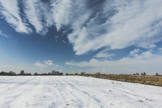 Snow on the field and fancy white clouds on the sky, winter view