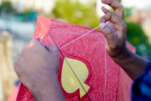 Man threading a paper and wood kite in order to fly it on the indian harvest festival of makar sankranti or uttarayana. This festival is known for its colorful kites of paper and wood used for kite fighting with a glass covered thread to cut an opponents kite