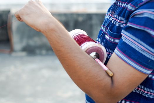 Man holding a charki phirki thread spool in the crook of his elbow and winding it with the other hand to ensure taughtness for the famed kite fighting festival of makar sankranti uttarayana This festival is known for its colorful kites of paper and wood used for kite fighting with a glass covered thread to cut an opponents kite