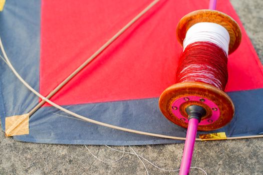 Top down flatlay shot with red and black paper and wood kite with a wooden handmade charkhi thread spool with normal and glass covered thread for kite fighting on teh indian festival of makar sankranti uttarayana . This festival is known for its colorful kites of paper and wood used for kite fighting with a glass covered thread to cut an opponents kite