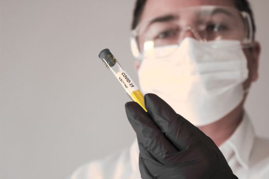 Madrid, Spain- November 25, 2020: Laboratory assistant wearing protective glasses and surgery gloves holding test tube of Covid-19 virus vacine