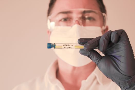 Madrid, Spain- November 25, 2020: Laboratory assistant wearing protective glasses and surgery gloves holding test tube of Covid-19 virus vacine