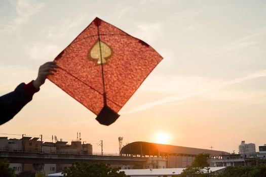 Young man holding aloft colorful paper and wood kite against a blurred background setting sun on the indian kite festival of makar sankranti or uttarayana. This festival is known for its colorful kites of paper and wood used for kite fighting with a glass covered thread to cut an opponents kite