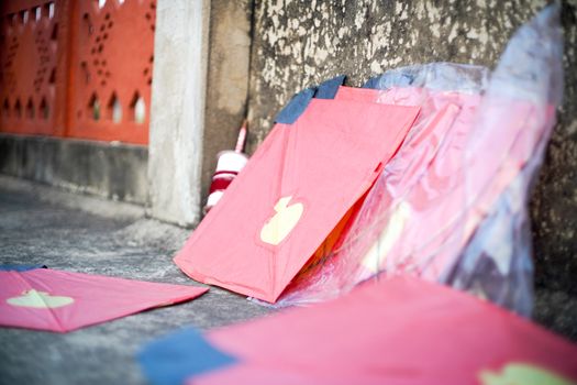 series of colorful red yellow paper and wood kits placed near fikri charki spools filled with dor plain thread and manjha glass covered thread for the indian festival of makar sankranti uttarayana . This festival is known for its colorful kites of paper and wood used for kite fighting with a glass covered thread to cut an opponents kite