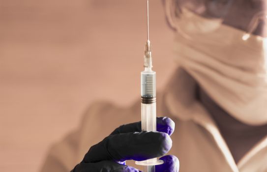 Laboratory assistant wearing protective glasses and surgery gloves holding a syringe with Covid-19 virus vaccine