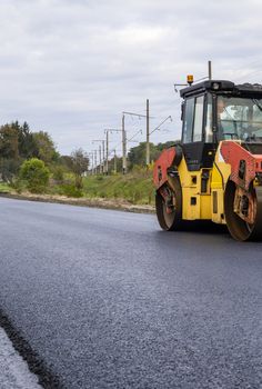 Asphalt road roller with heavy vibration roller compactor press new hot asphalt on the roadway on a road construction site. Heavy Vibration roller at asphalt pavement working. Repairing