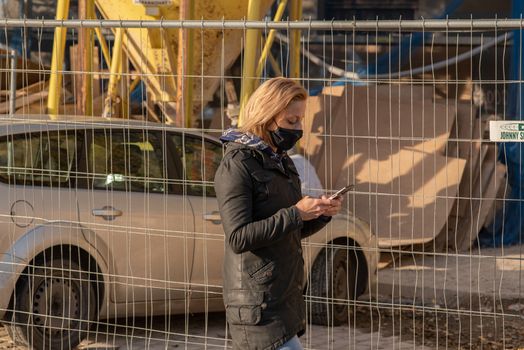 11-23-2020. Prague, Czech Republic. People walking and talking outside during coronavirus (COVID-19) at Hradcanska metro stop in Prague 6. Woman with mask looking her phone.