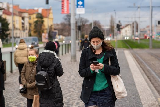 11-23-2020. Prague, Czech Republic. People walking and talking outside during coronavirus (COVID-19) at Hradcanska metro stop in Prague 6. Woman with mas waiting for tram..