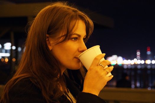 the girl drinks coffee on the street in the evening.