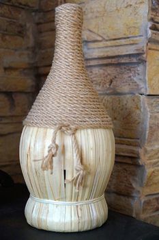 bottle decorated with jute rope and straw against a stone wall.