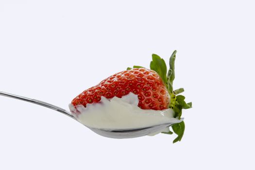 Red strawberries with green leaves in a spoon of sour cream against white background
