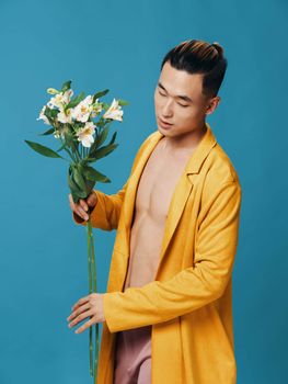 Side view of cute Asian guy with a bouquet of flowers on a blue background. High quality photo