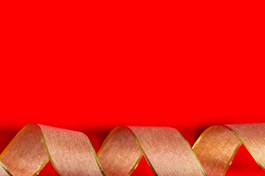Golden ribbon against red background. gold packaging ribbon curls on red background, new year background, copy space, place for text, banner, holiday concept, Christmas, new year, Valentine's day.