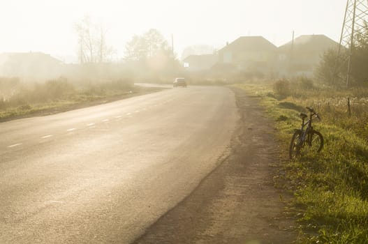 Sunset in the background of the road and fields with grass and trees.