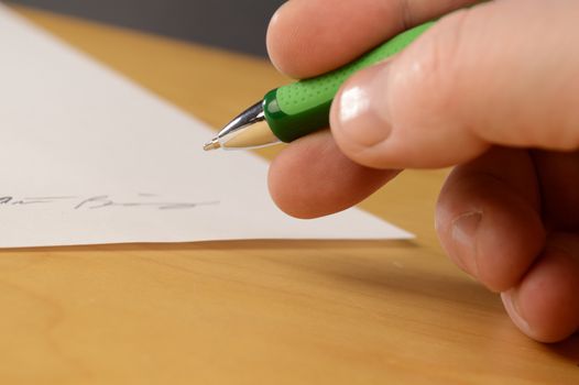 An important document is being signed by the appropriate person with a closeup of their hand and focus on the tip of the ball point pen.