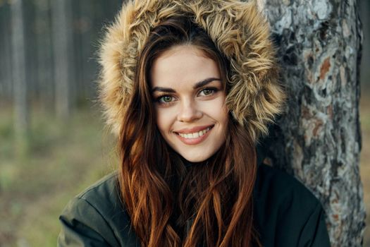 Woman in a jacket with a hood near a tree on a forest background cropped view. High quality photo