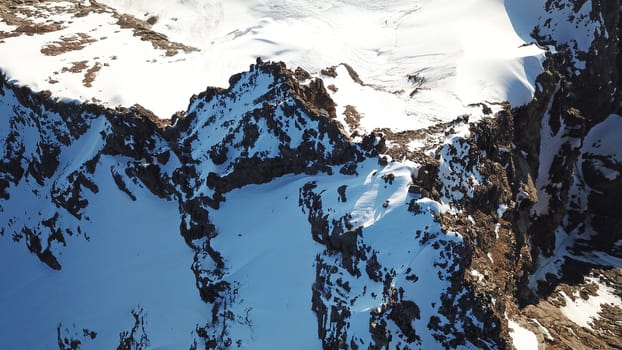 People on the top of a snowy mountain. Top view from a drone. Huge rocks covered with snow, climbers stand on top of the peak. Extreme rest. Steep slopes where there may be an avalanche. Highest peak