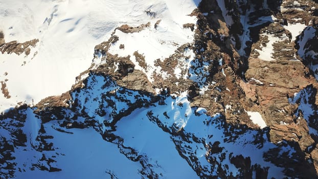 People on the top of a snowy mountain. Top view from a drone. Huge rocks covered with snow, climbers stand on top of the peak. Extreme rest. Steep slopes where there may be an avalanche. Highest peak