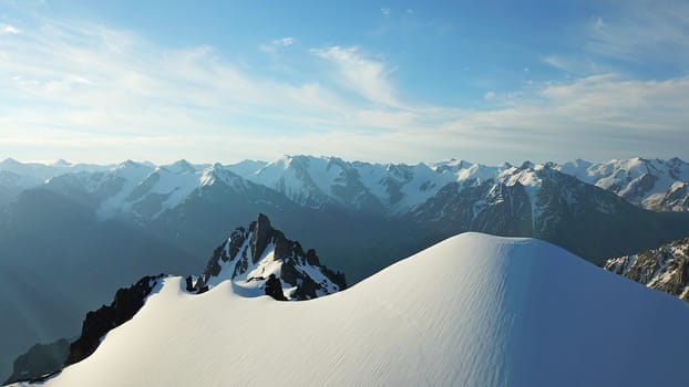 People on the top of a snowy mountain. Top view from a drone. Huge rocks covered with snow, climbers stand on top of the peak. Extreme rest. Steep slopes where there may be an avalanche. Highest peak