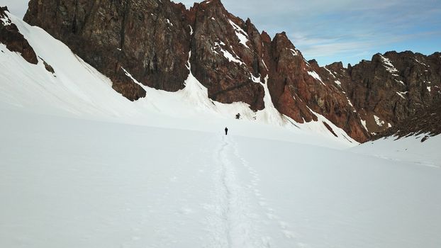 A large group of climbers climb to the top. A camp of tents is set up. Snowy mountains in summer. View of the trail with a group of tourists. Queue for the peak. Shooting from above from a drone.