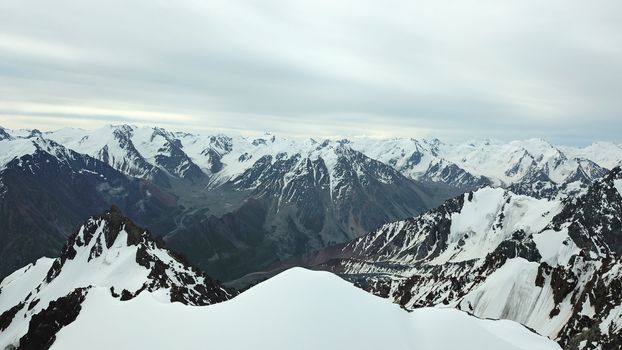 Huge snow mountains. View from the top of the drone. In places, you can see small people climbing to the top. Panorama of steep peaks and rocks, snow cornices. Mountaineering class. Extreme rest.