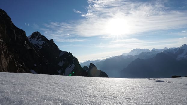 Dawn in the snow-capped mountains. View of the bright sun, mountains and rocks, snow cornice. Snowflakes fly, clouds float. The height is more than 4000 meters. TRANS-Ili Alatau, Kazhastan.