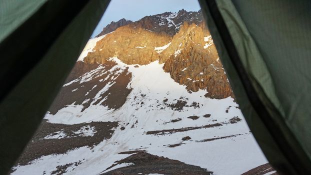 View from the tent-tent on the snow-covered mountains. The edges of the tent, the castle and the view of the rocky slopes covered with snow. Sun ray. Mountaineering camp in the mountains. Almaty.