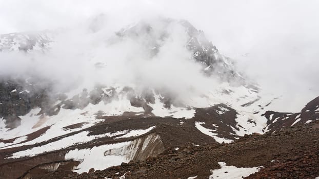 White clouds and snowy peaks. A lot of big stones. Steep cliffs, sometimes covered with white snow. Clouds float through the mountain tops. Moss grows in places. Mountains of the TRANS-ili Alatau.