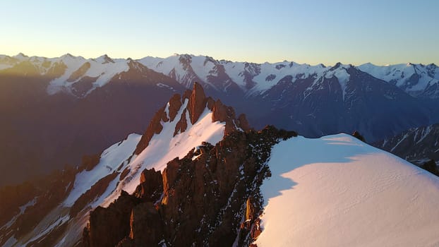 Epic red dawn on top of snowy mountains. Top view from a drone. Huge rocks covered with snow, the ledge of snow overhangs. An avalanche-prone place. Climb to the peak. Flying above the peak. Almaty